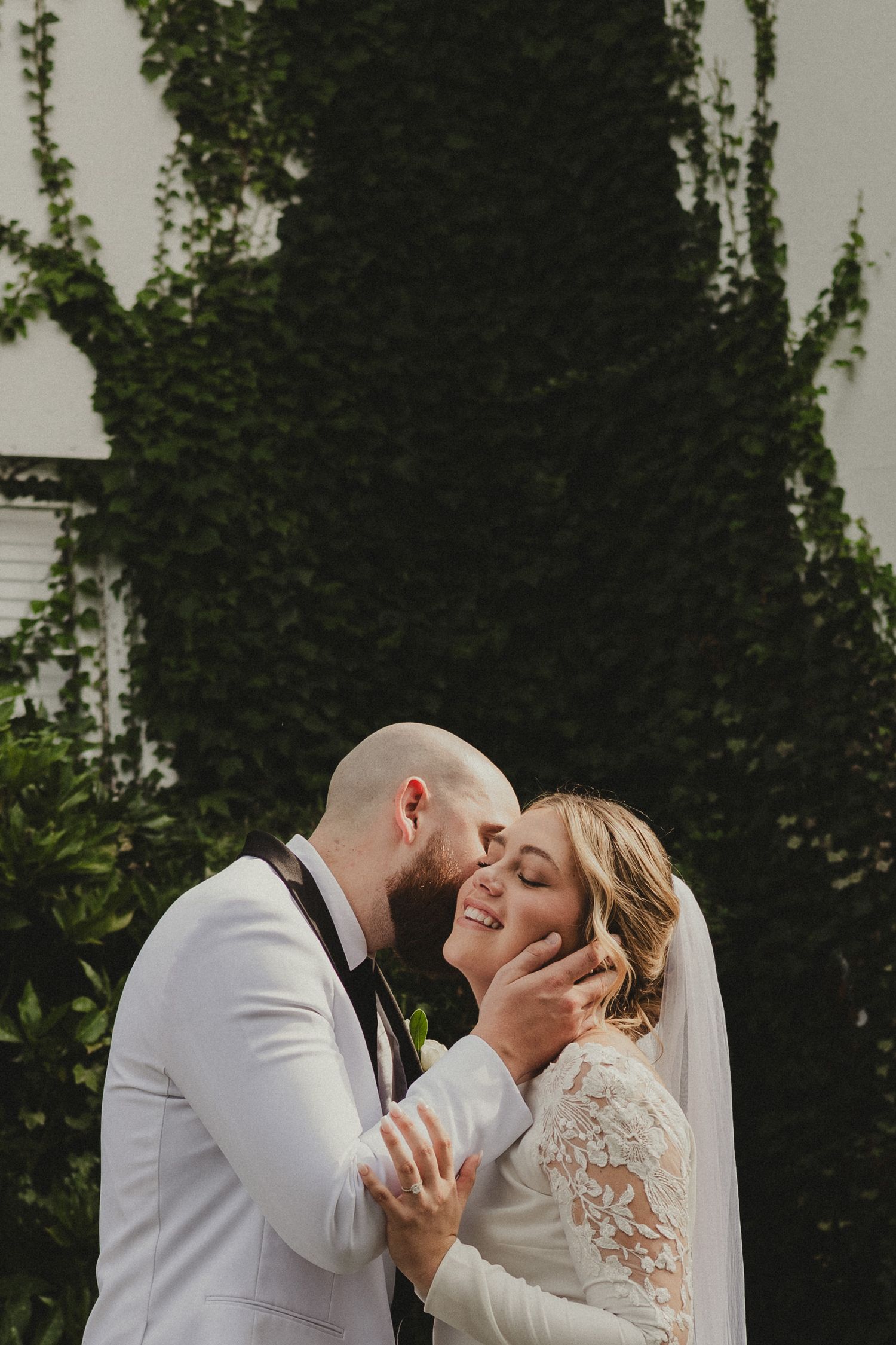 A romantic bride and groom share their first kiss during a wedding ceremony against a lush green backdrop.