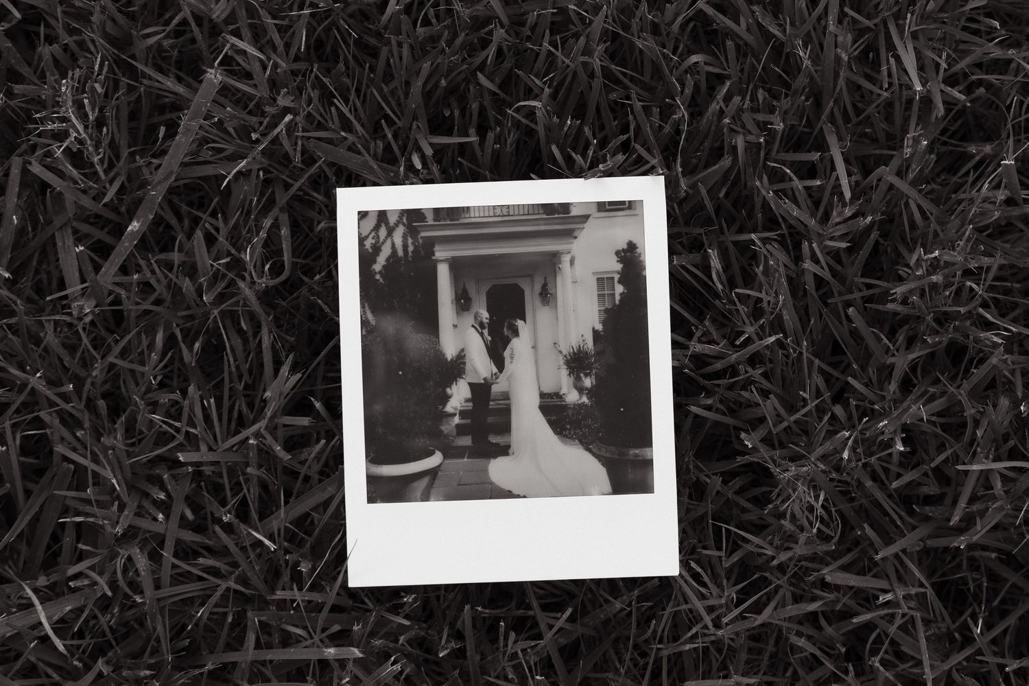 A black and white Polaroid photograph of a walkway with columns lies on grass.