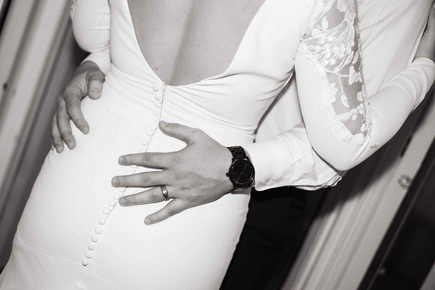 Black and white close-up photo showing embracing couple with hands on waist wearing formal white wedding attire.