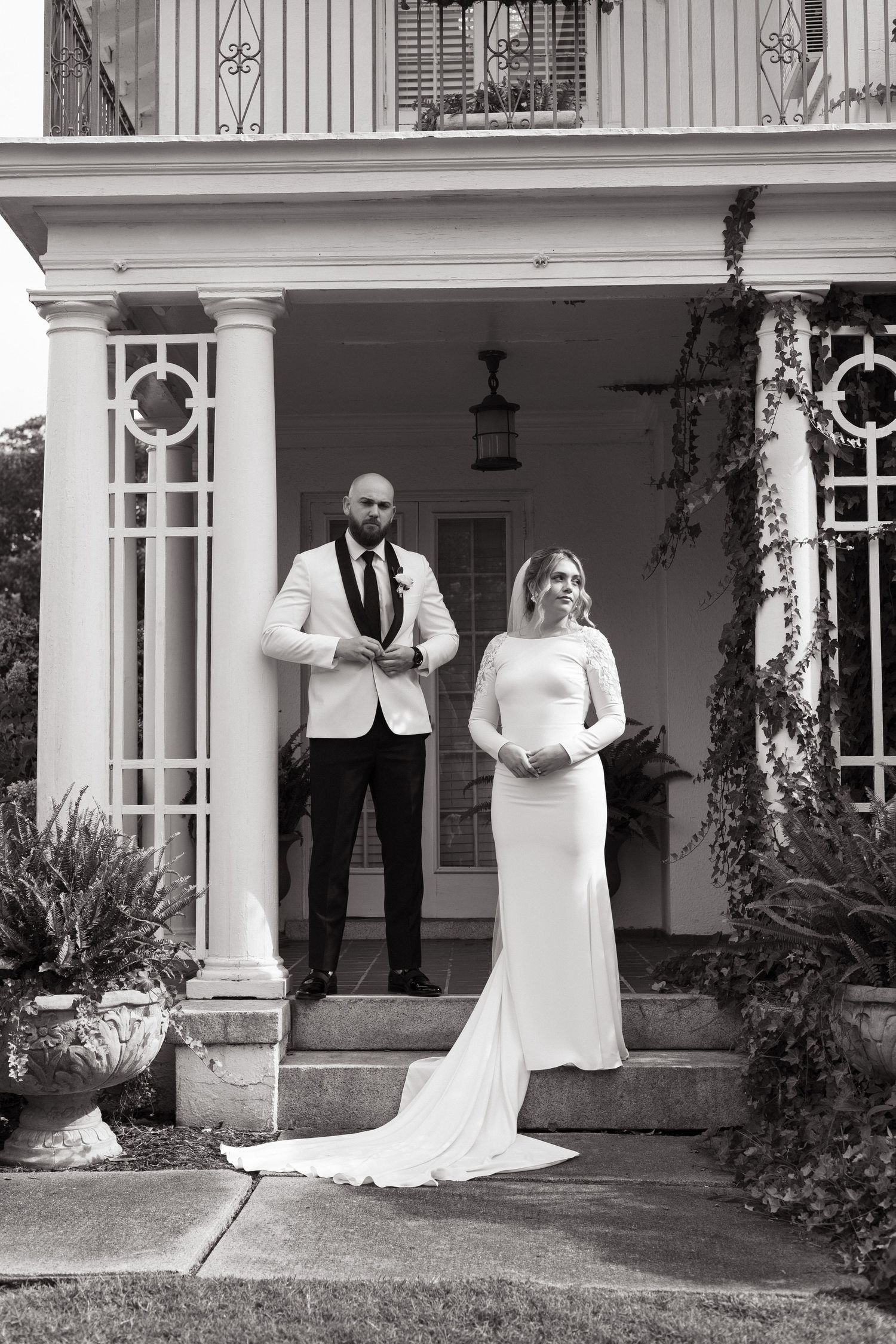 A couple poses together on an elegant white porch with classical columns at their formal event.