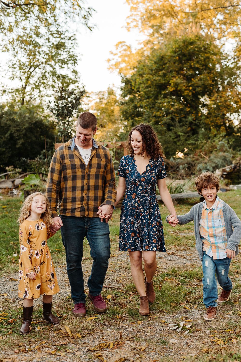 A family takes an autumn stroll together on a leaf-covered path through a garden while wearing coordinated casual outfits.