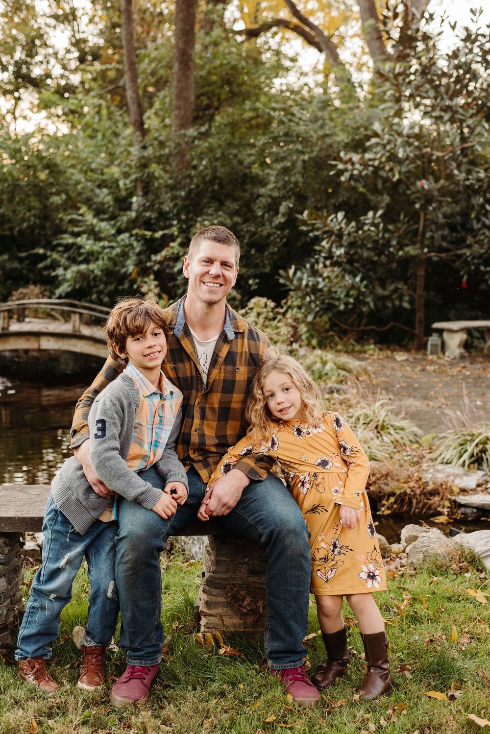 A family sits together on grass during a golden autumn photoshoot wearing coordinated casual outfits.