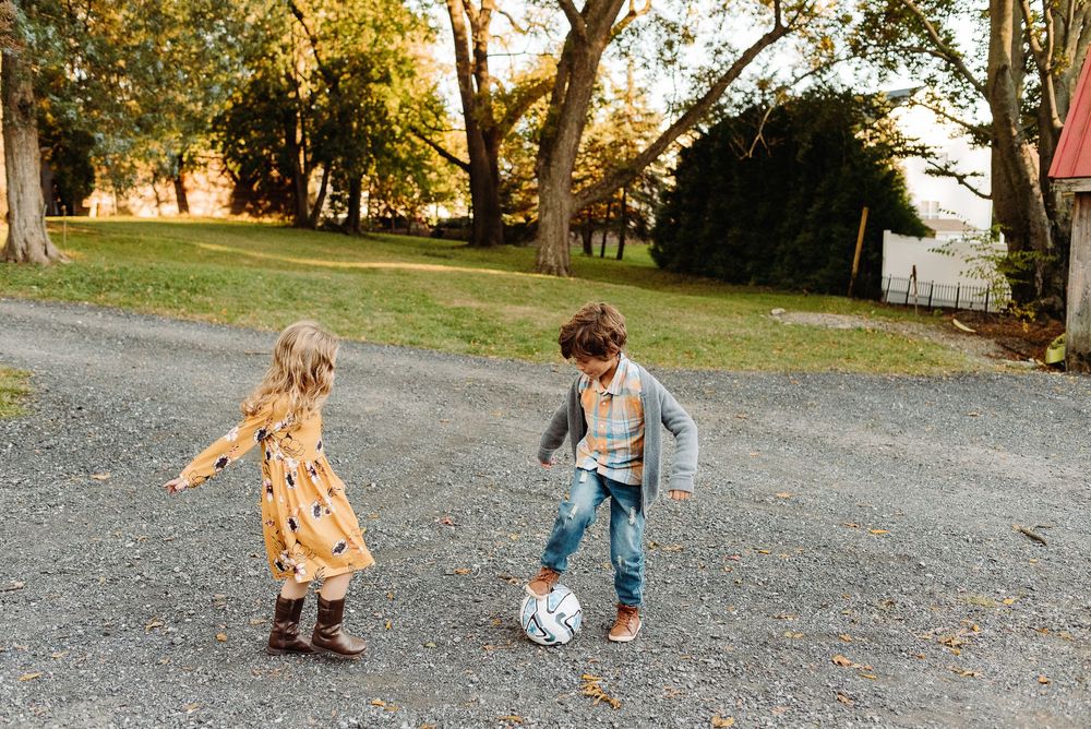 Children playing in fallen leaves on a gravel driveway during autumn.