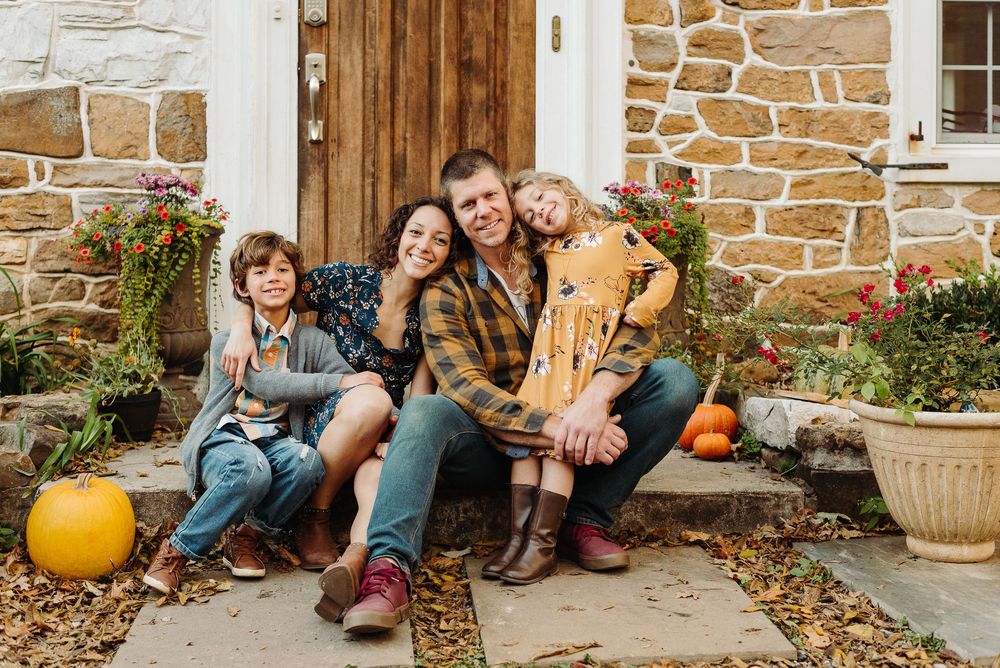 People sitting on stone porch steps with autumn pumpkins in front of rustic stone house exterior.