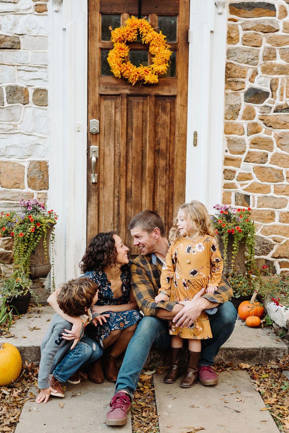 Fall decorations adorn a wooden door entrance with orange wreath and pumpkins on stone house steps.