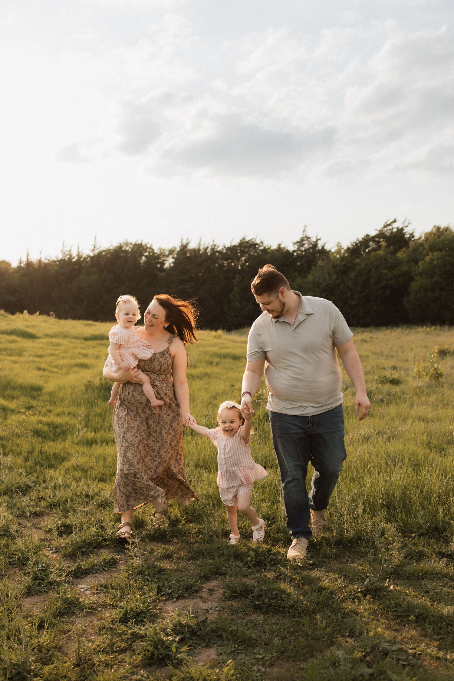 Family walking together in a sunlit grassy meadow during golden hour with trees in background.