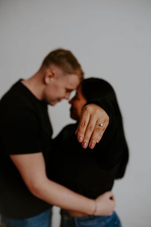 An intimate black and white studio portrait showing a couple embracing with focus on an engagement ring.
