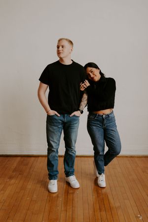 A casual engagement photo showing a couple in matching outfits sitting on a wooden floor.