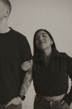 Couple in dark clothing share intimate poses against neutral backdrop in minimalist style.