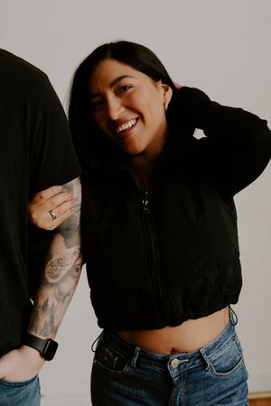 Woman in black crop top and jeans poses playfully against white wall showing candid expressions.