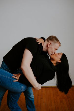 Couple embracing and leaning together on wooden floor in artistic black and white photography.