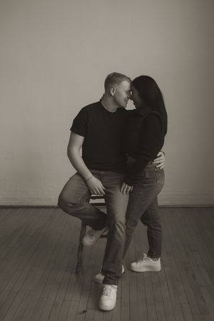 Couple in casual wear sitting close together on wooden floor in intimate portrait session.