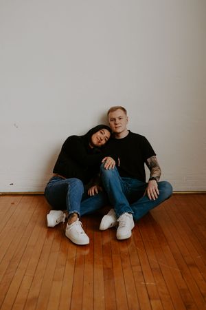 Two people relax together on wooden floor in casual attire.