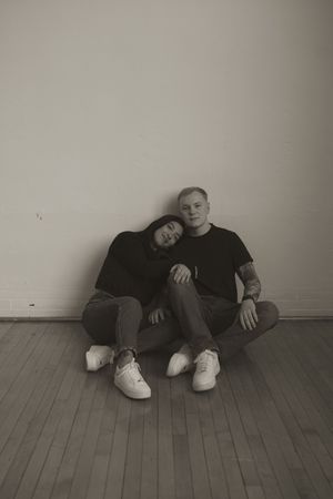 Couple rests together on hardwood floor in monochromatic setting.