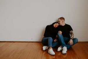 Couple relaxes together against minimalist white wall setting.