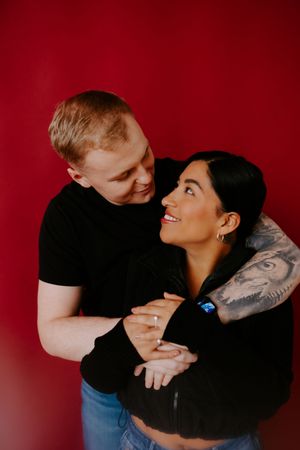 Intimate couple portrait against red background showing playful affection.