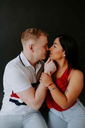 Couple in white and red outfits sharing intimate moment against dark background.