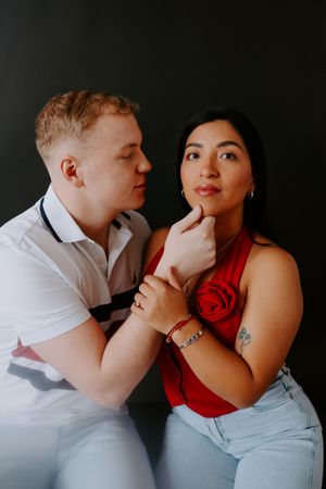 Couple in contrasting white and red outfits sharing tender moment in dark studio.