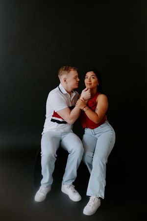 Artistic couple portrait against black background showing playful interaction.