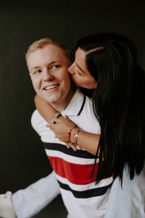 Playful couple embraces while wearing white and red clothing against dark backdrop.