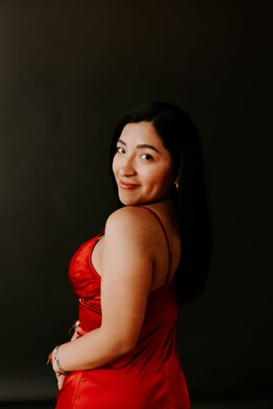 Woman in a red dress poses confidently against a dark background with a joyful expression.