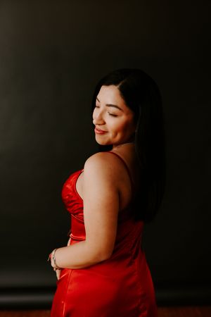 Woman in red dress poses elegantly against dark background during portrait session.