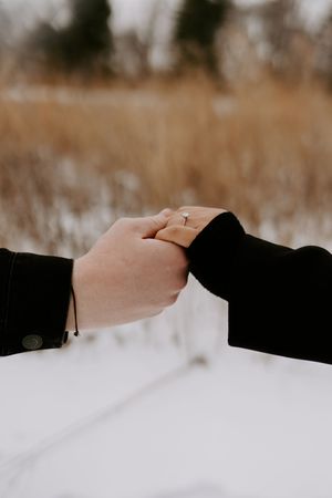 Close-up of hands reaching toward each other in snowy winter setting.