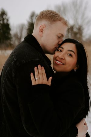 A romantic winter engagement photo session showing an intimate close-up moment between a couple in black coats.