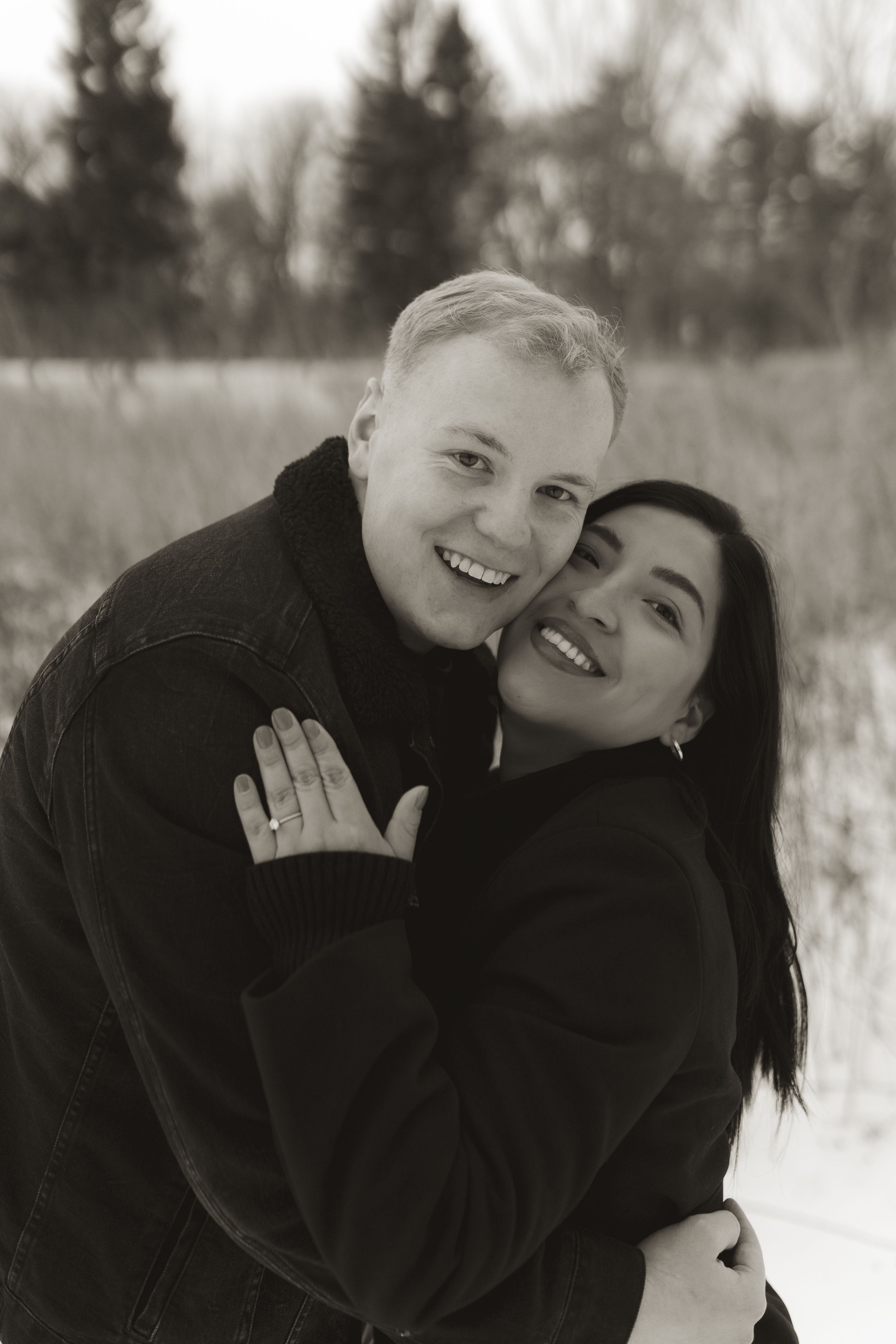 A couple sharing intimate moments and laughter during a winter photoshoot in a snowy field.