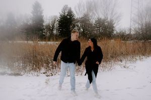 Silhouettes of two people walking through a snowy winter landscape with trees in the background.