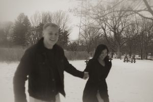 A couple runs playfully through the snow in a winter landscape.