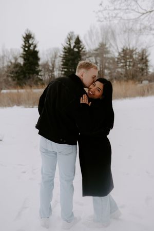 A couple shares a playful moment against a snowy winter backdrop.
