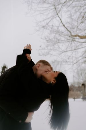 Romantic winter photoshoot showing silhouettes of a couple against bare tree branches.