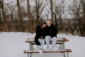 A couple sharing romantic moments on a bench in a snowy winter setting.