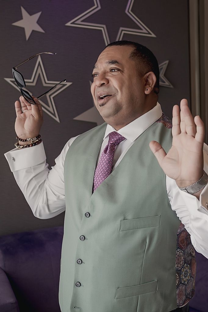 Stylish professional in mint green vest and purple tie gestures expressively against wall decorated with silver stars.