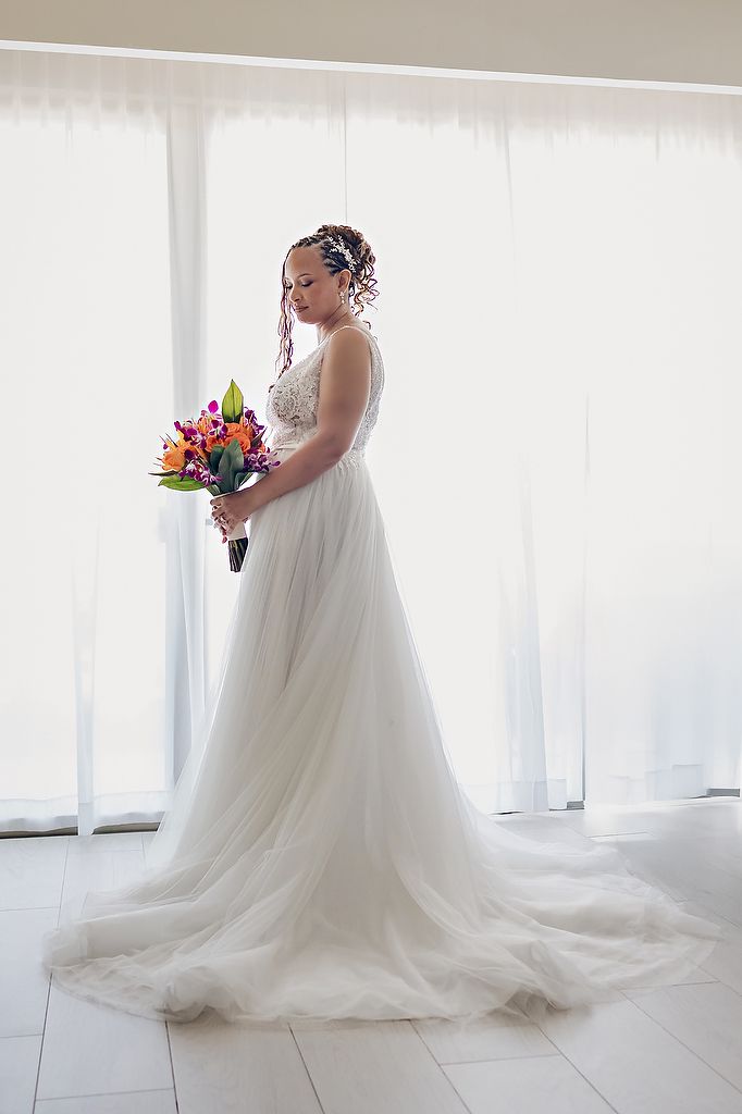 A bride in a flowing white gown holds a vibrant bouquet against a light-filled backdrop.