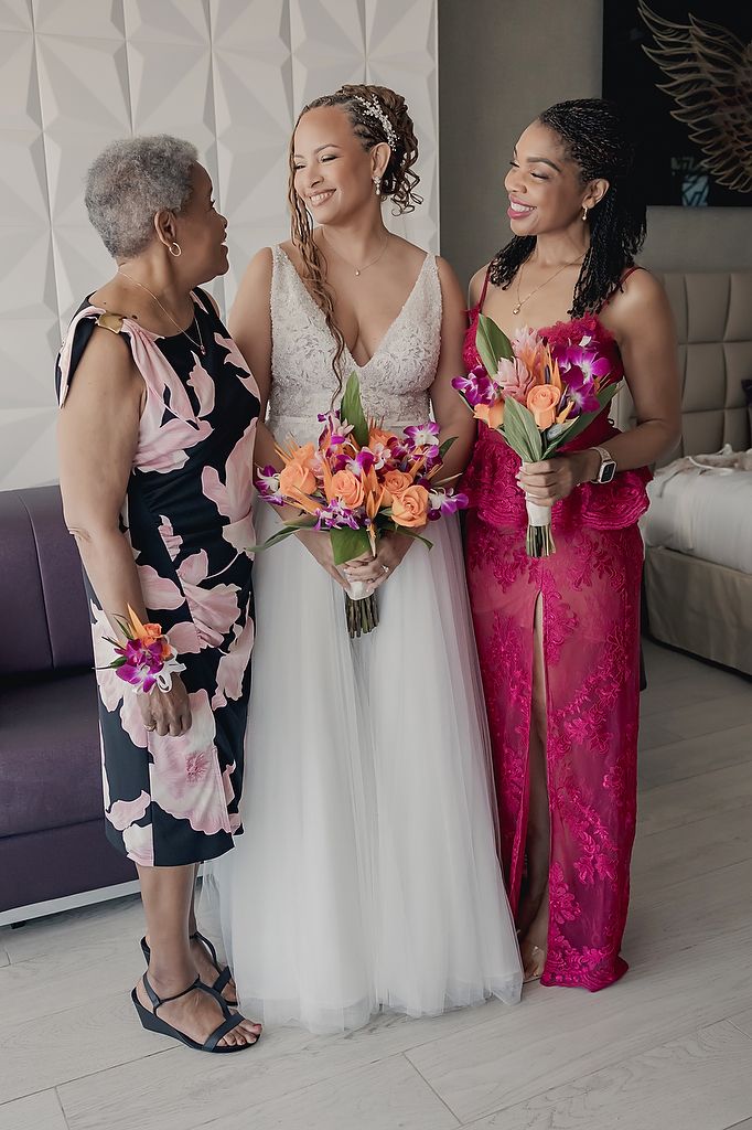 A joyful wedding scene with three generations sharing laughter while holding vibrant pink and orange bouquets.
