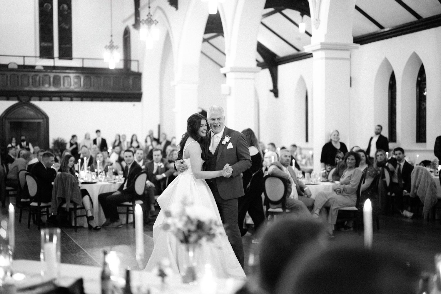A couple shares their first dance at an elegant church wedding reception with guests seated at tables in black and white.