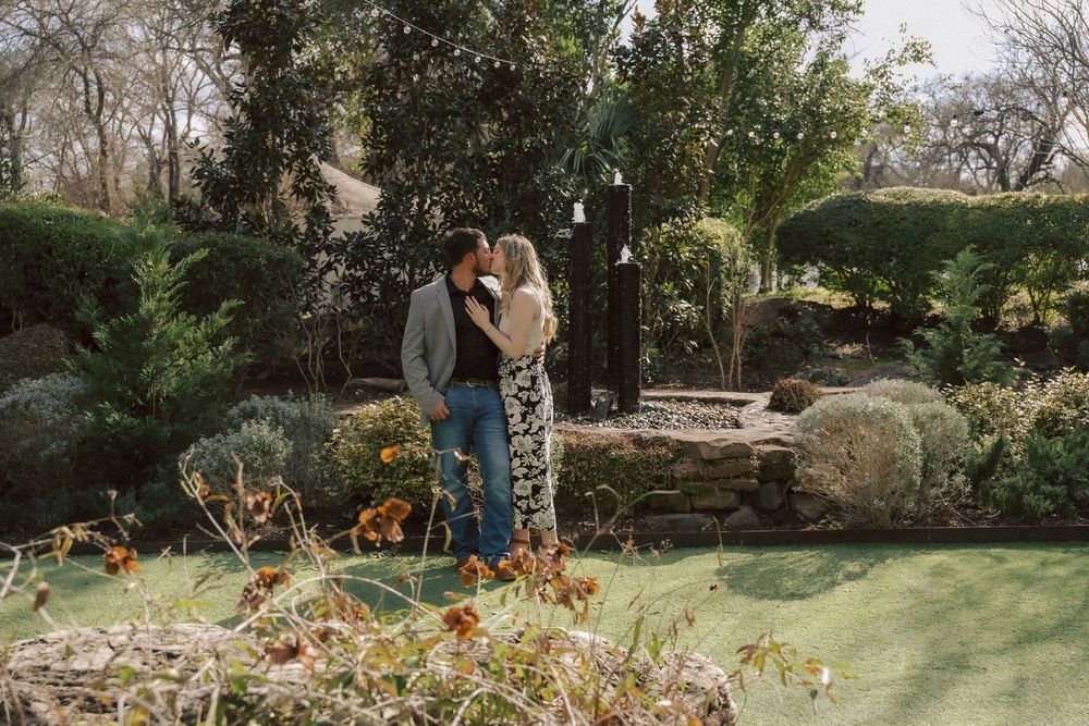 Two people stand together in a peaceful garden setting with landscaped rocks and autumn flowers.