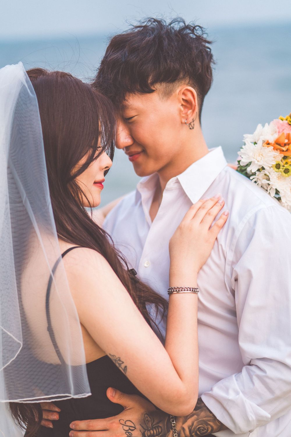 Intimate close-up of couple in wedding attire against ocean backdrop.