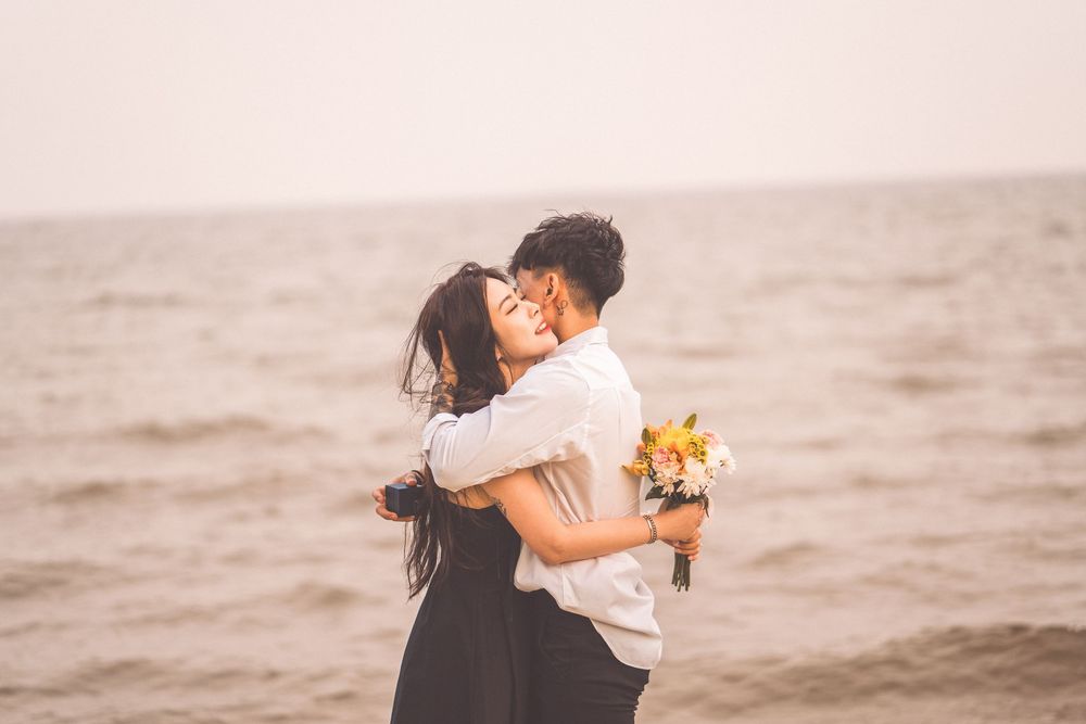 Romantic embrace on beach with bouquet of flowers.
