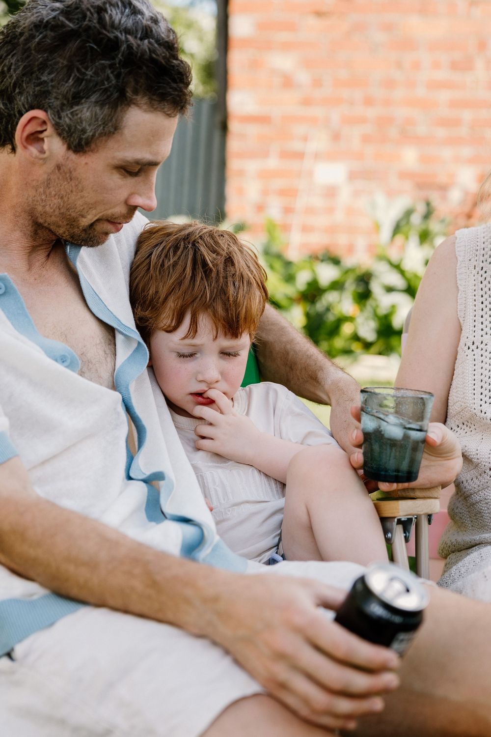 Casual outdoor scene with adult and young child relaxing together as they share beverages on patio furniture.