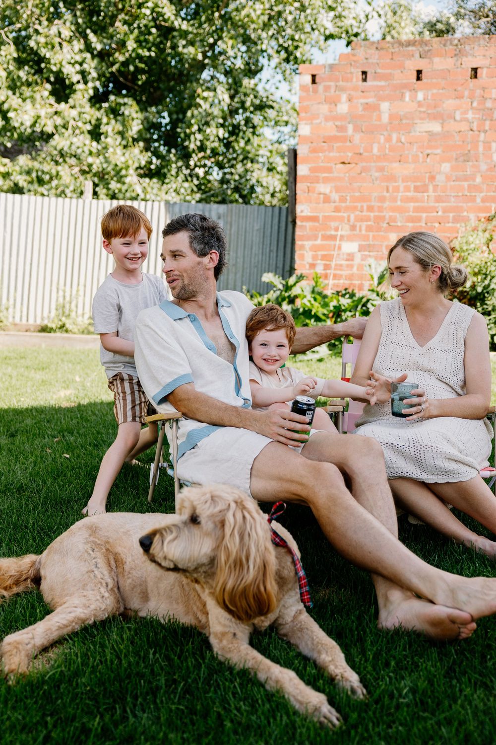 Family enjoying drinks together on a summer day in backyard with their golden retriever dog lying on grass.