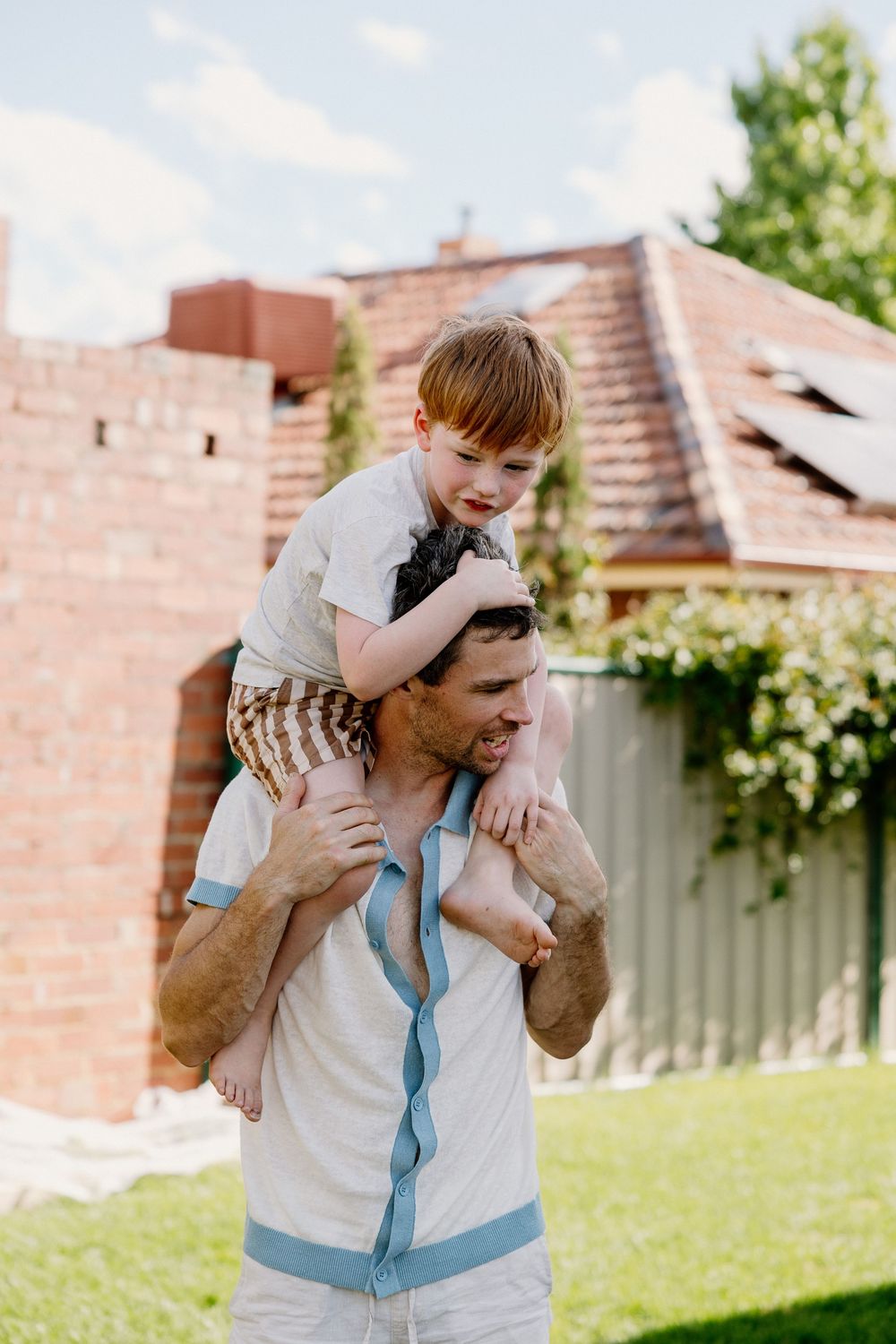 Parent and child share a joyful playful moment while piggyback riding in a sunny backyard with brick wall backdrop.