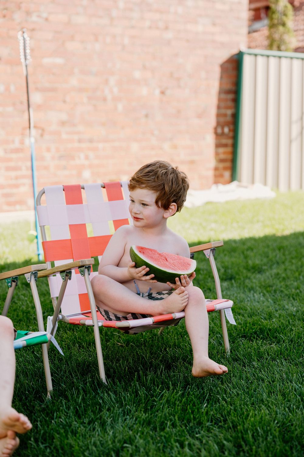 Children playing on a row of colorful lawn chairs in a backyard.