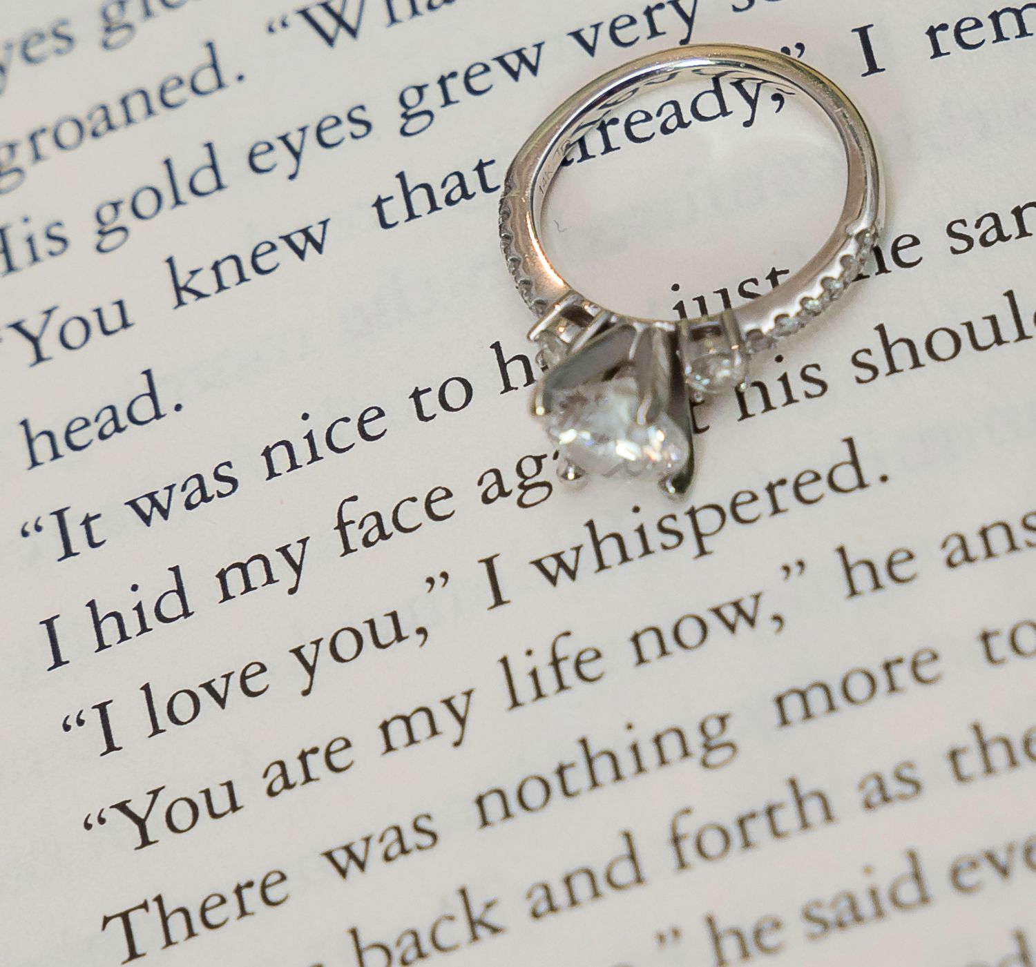 Wedding rings photographed on pages of a romantic book with text visible beneath.
