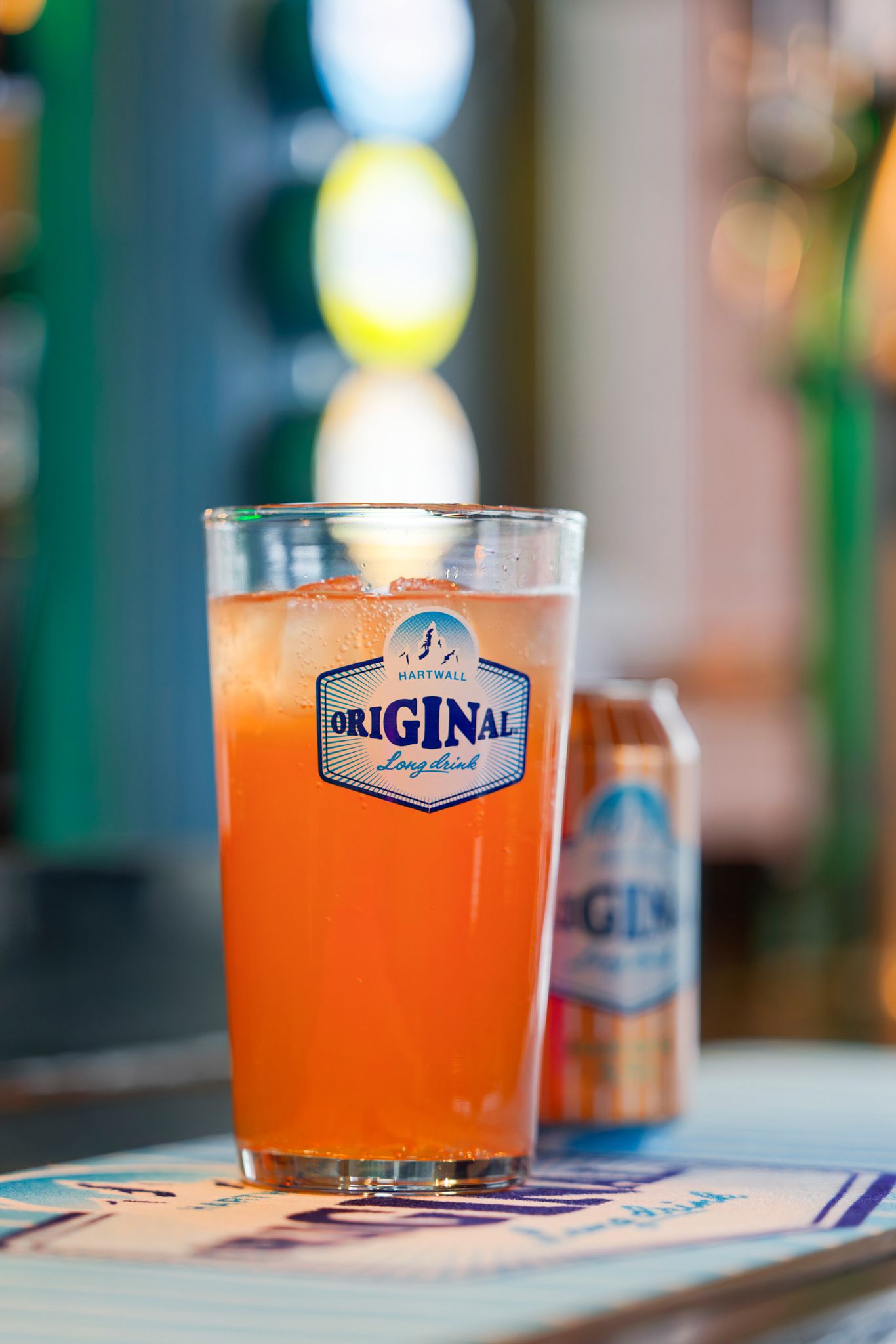 A glass of Hartwall Original Long Drink cocktail beside its can on a bar counter.
