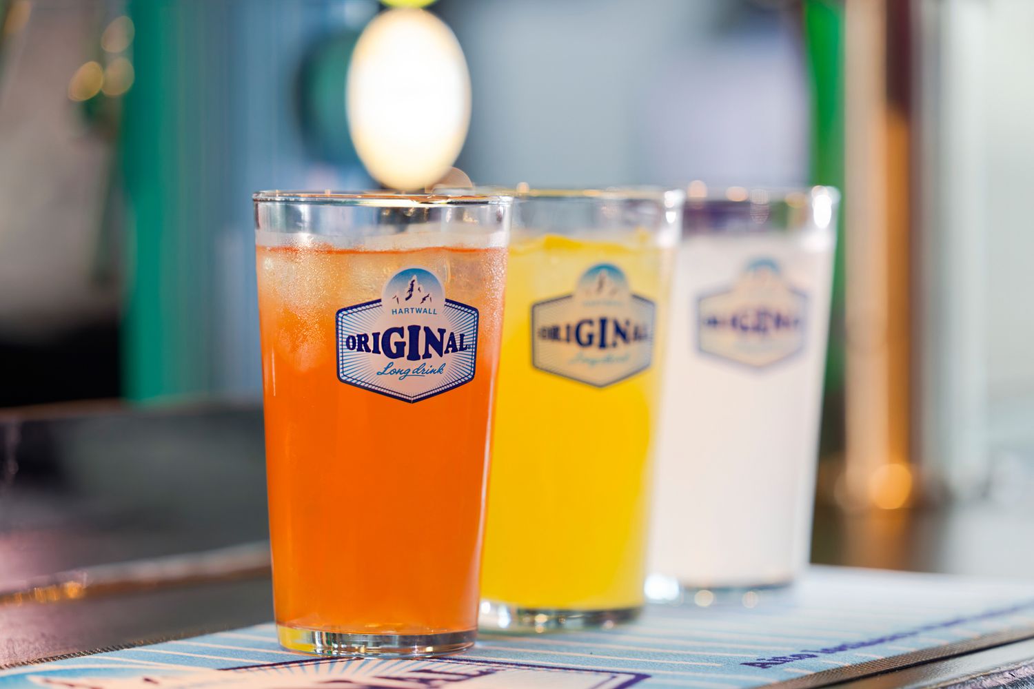 Three Original-branded pint glasses filled with colorful craft beers displayed on a bar counter.