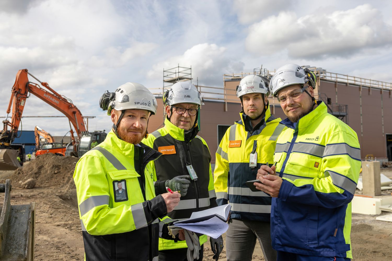 Construction workers in high-visibility gear review project plans and documents at an outdoor worksite.