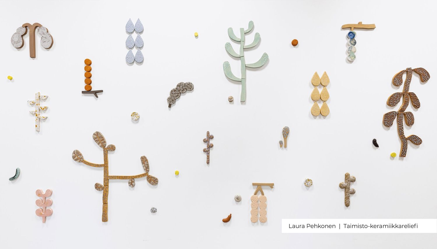 Abstract ceramic wall sculptures by Laura Heikkinen featuring tree and plant shapes in muted earth tones on a white gallery wall.
